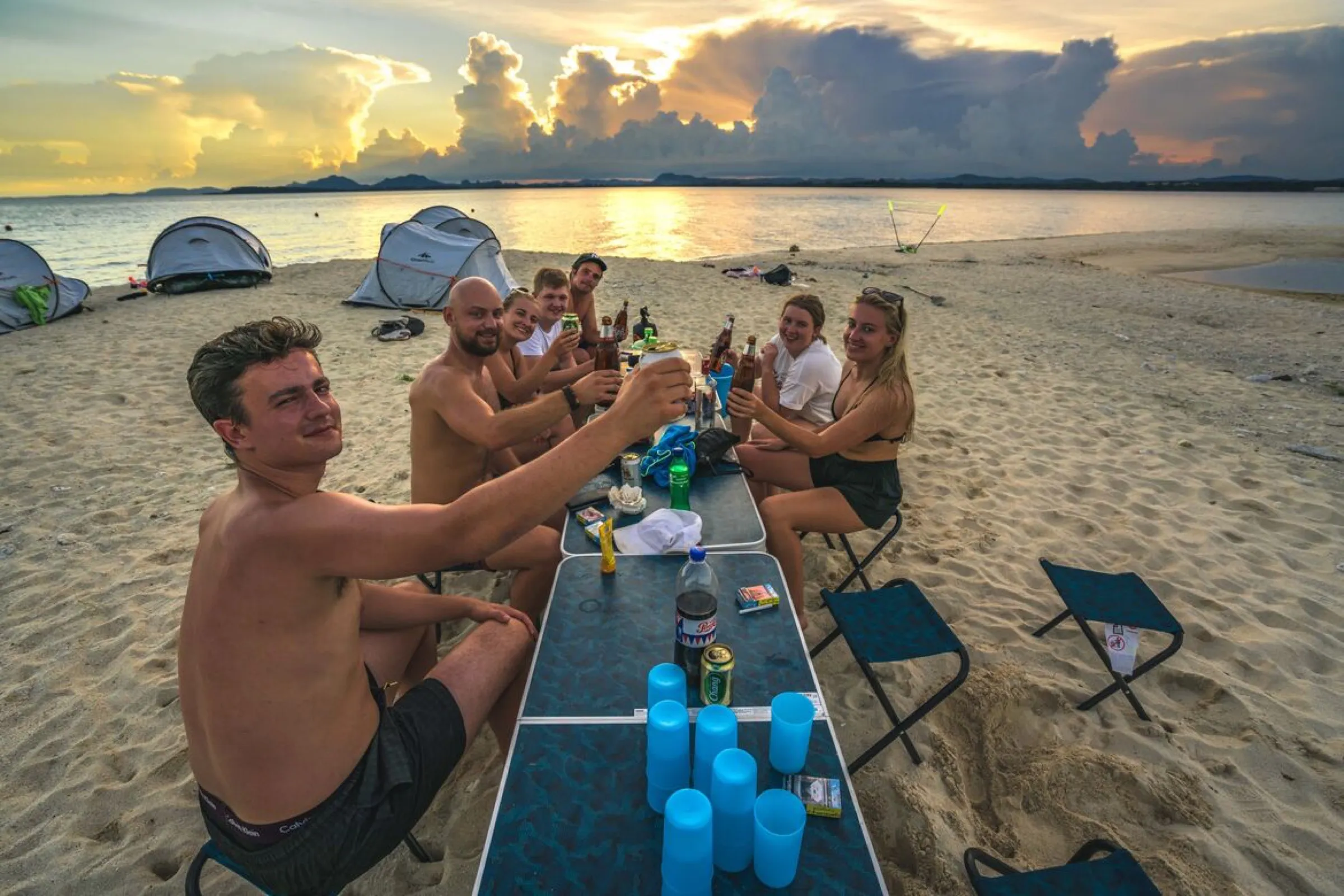 A group raising a toast on the beach at golden hour, Koh Kye, Thailand.