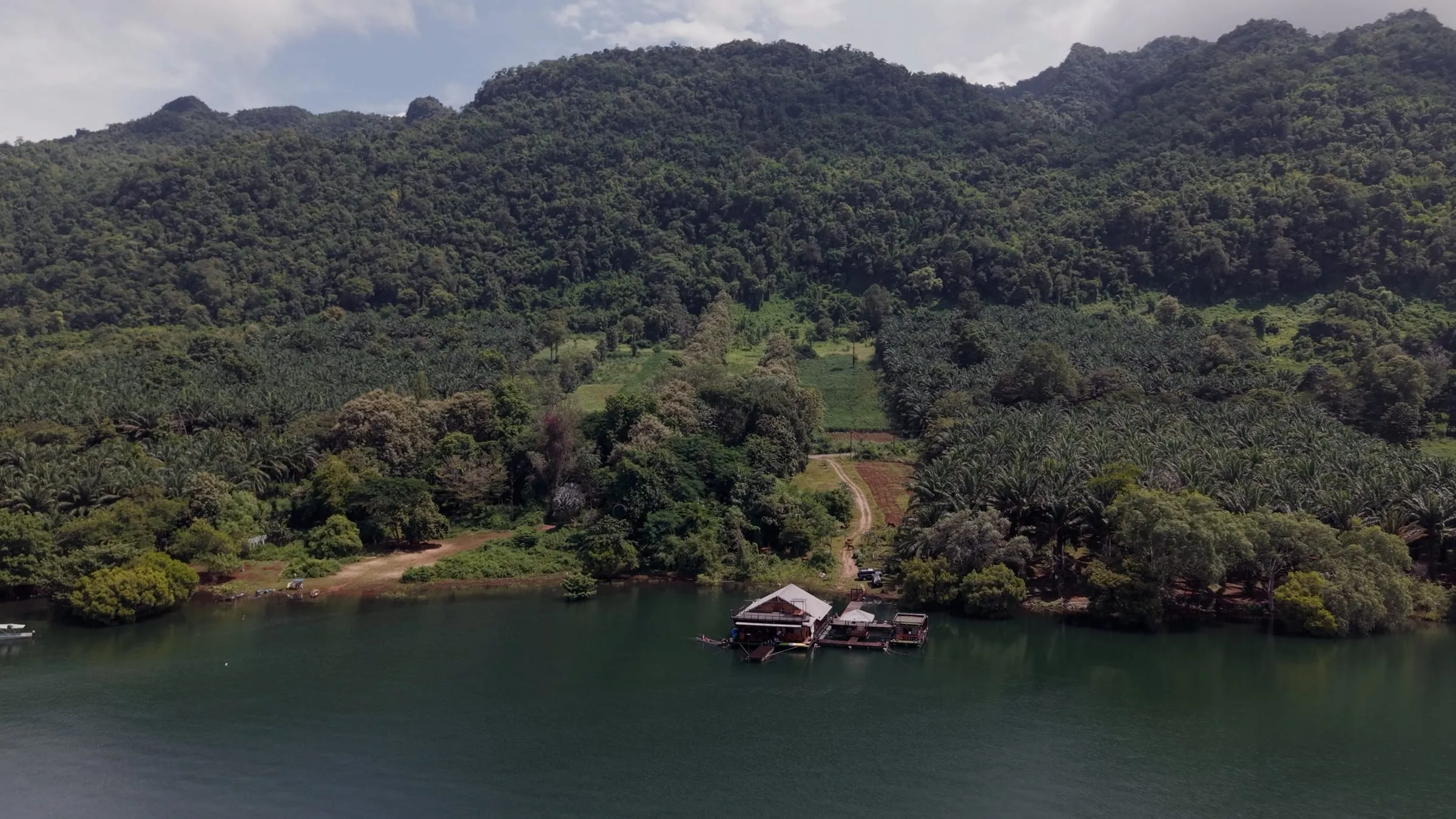 Aerial of a floating house tucked against the forested shore of Khao Laem Lake, Thailand.