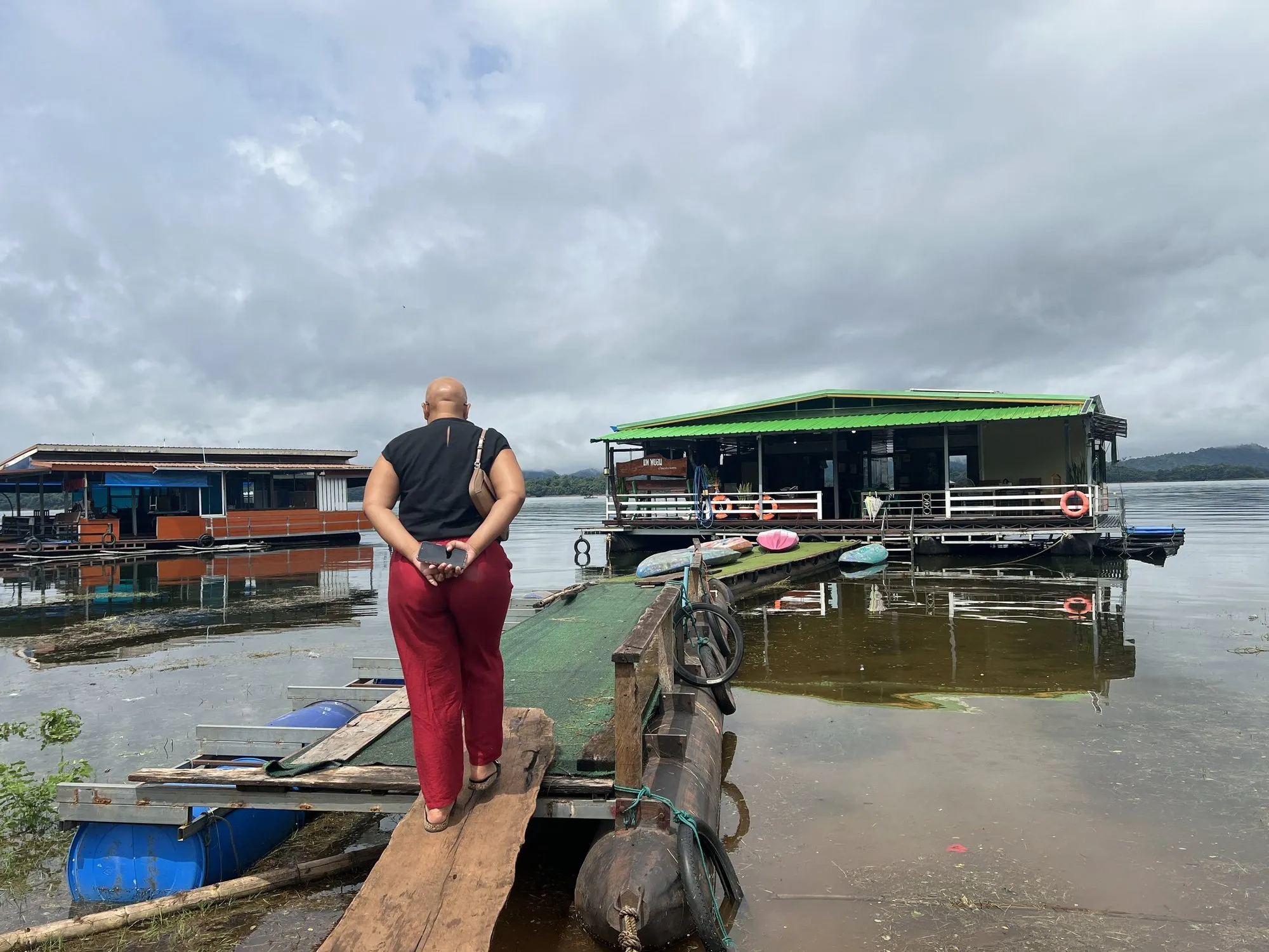 A visitor walking down the wooden gangway onto a moored raft house, Khao Laem Lake, Thailand.