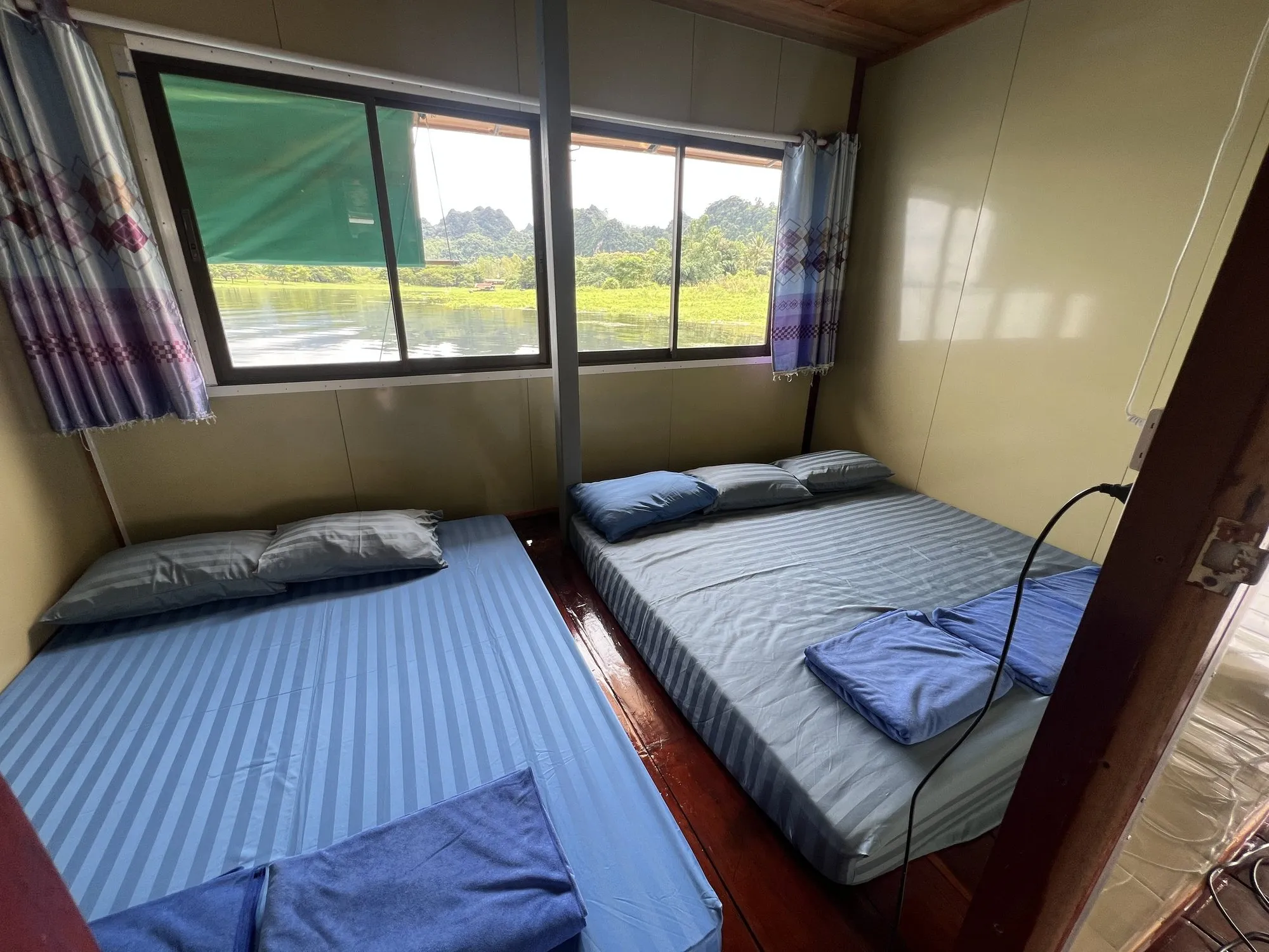 A simple private room on a raft house with mattresses on a low platform and a window onto Khao Laem Lake, Thailand.