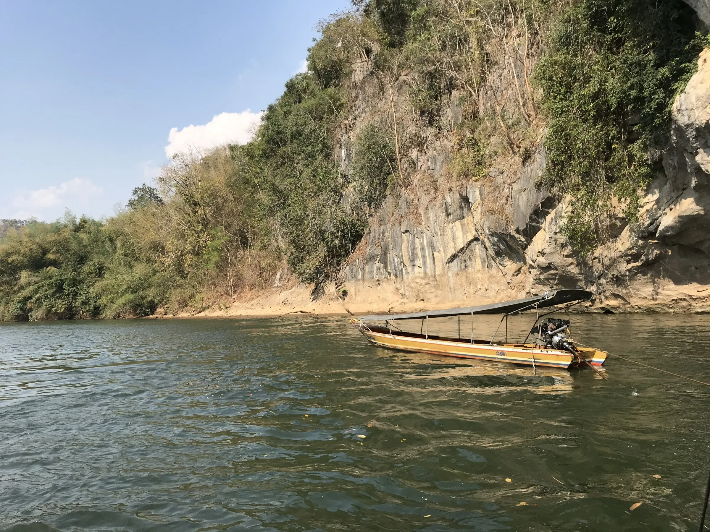 A longtail boat on the green River Kwai below limestone cliffs at Sai Yok, Thailand.