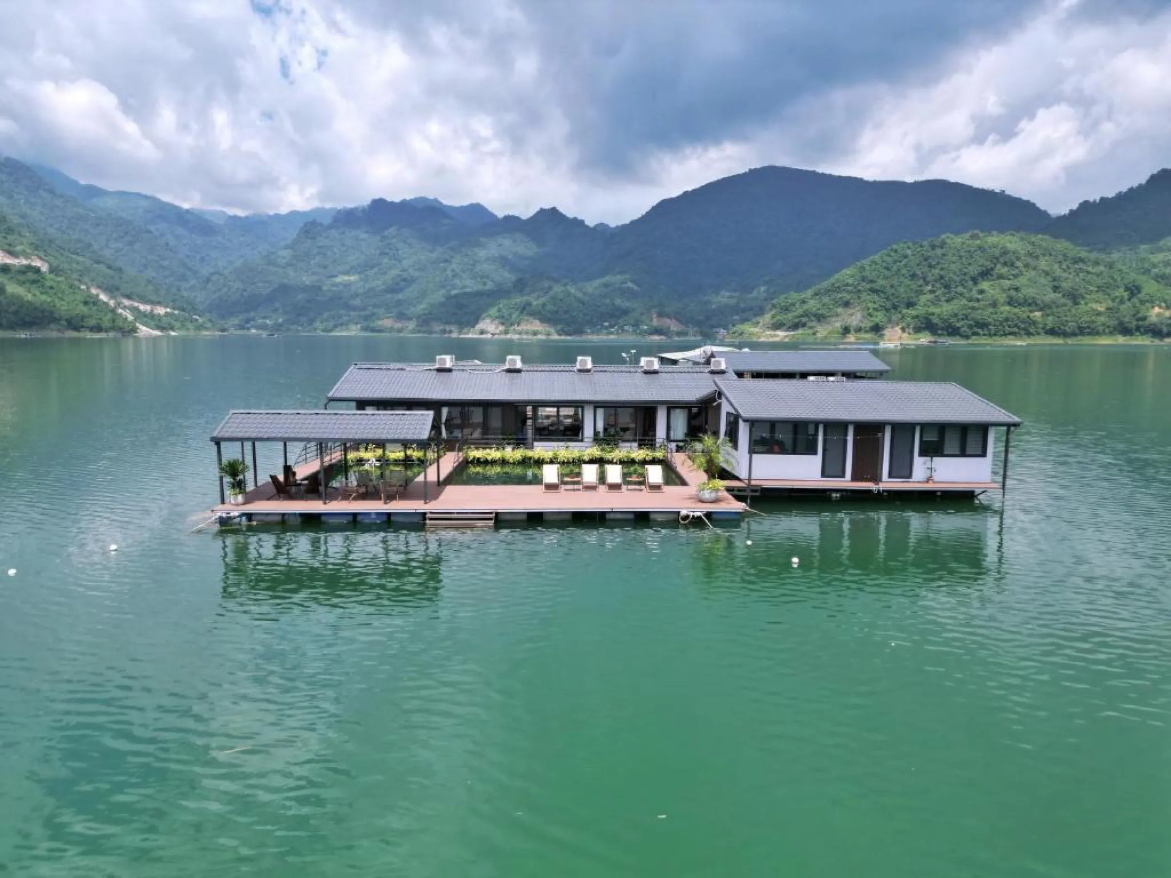 A private floating house moored on the calm jade water of Hoa Binh Lake, mountains behind.